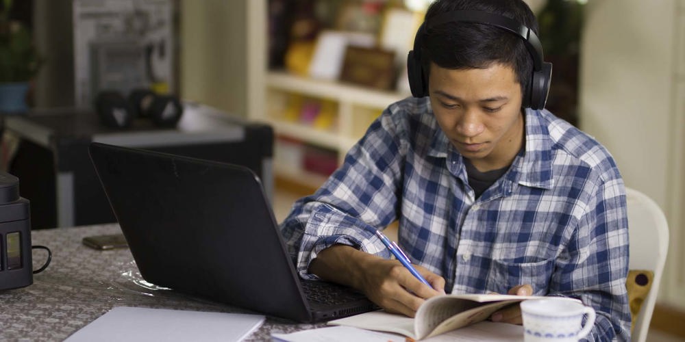 ung dreng der sidder med headphones og arbejder på computer.