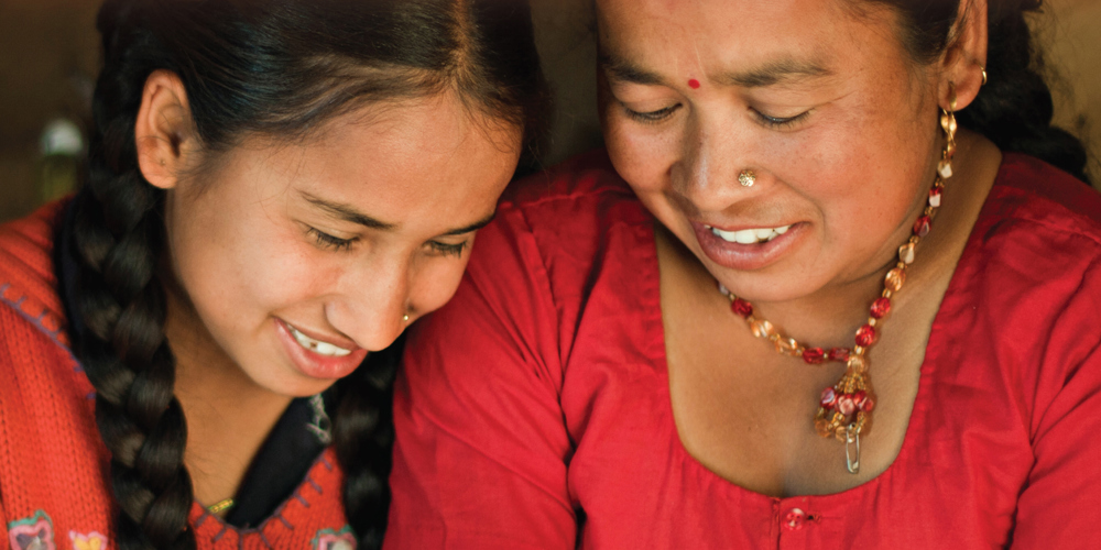 To sydamerikanske kvinder der sidder tæt og griner i rødt tøj.