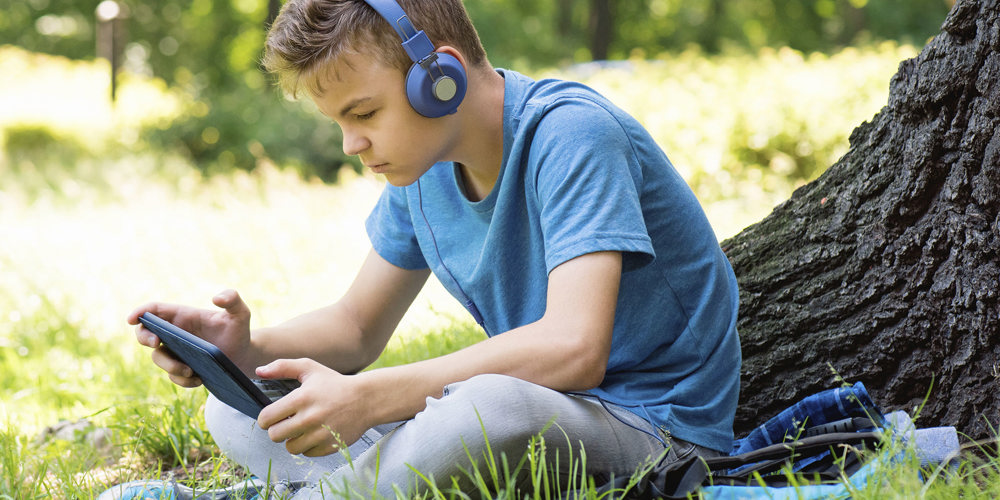 Dreng der sidder undertræ med headphones og Ipad.