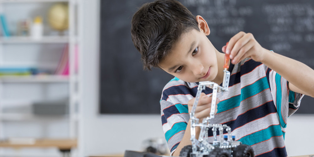 Dreng der sidder i klasselokale og bygger maskiner med klodser.